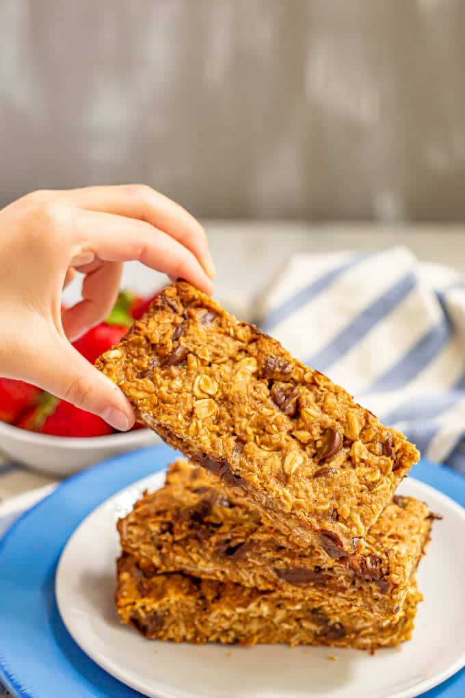 A stack of three granola bars on a plate with one being picked up