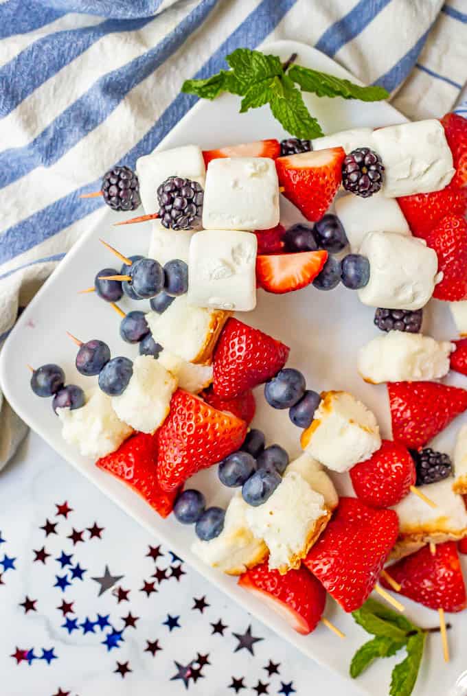 4th of July fruit kabobs stacked and arranged on a white platter with red white and blue decorations