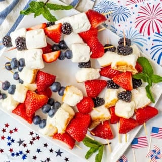 Platter full of red white and blue July 4th fruit kabobs and festive American decor nearby