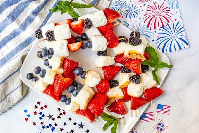 Platter full of red white and blue July 4th fruit kabobs and festive American decor nearby