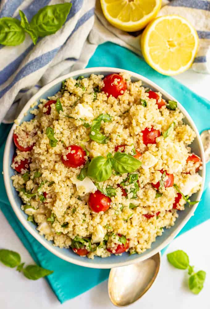 Salad of quinoa, tomatoes, mozzarella and basil with lemon vinaigrette served in a large bowl and fresh lemons in the background