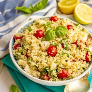 Quinoa Caprese salad with tomatoes, mozzarella and fresh basil served in a large bowl with lemons in the background