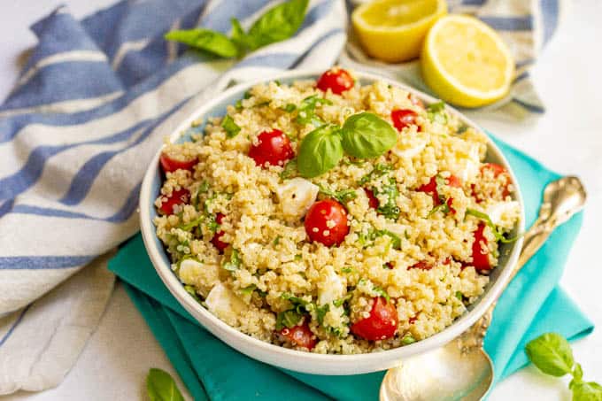 Quinoa Caprese salad with tomatoes, mozzarella and fresh basil served in a large bowl with lemons in the background