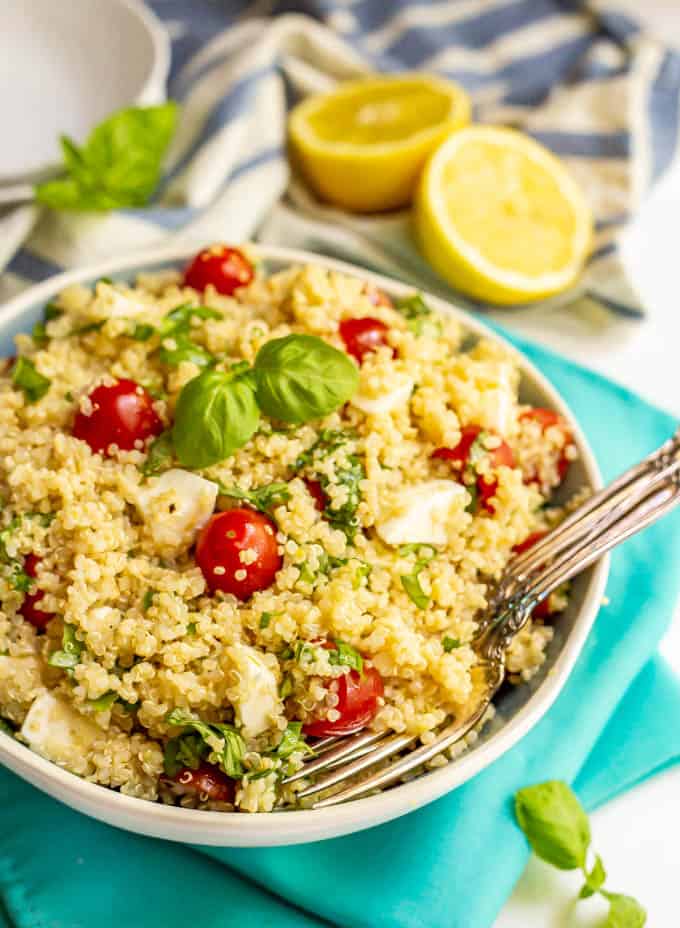 Quinoa Caprese salad with tomatoes, mozzarella and fresh basil served in a large bowl with lemons in the background