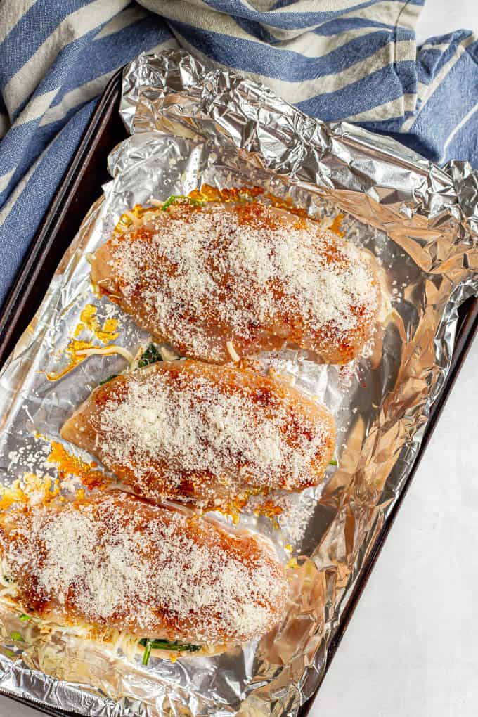 Chicken breasts topped with Parmesan cheese on a foil lined baking pan before baking