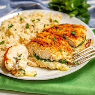 Sliced Parmesan crusted chicken breast stuffed with spinach and mozzarella cheese on a white plate with brown rice with a fork leaning on the plate