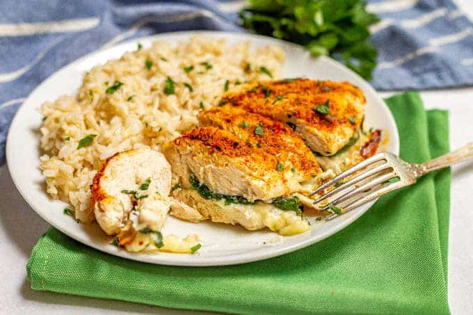 Sliced Parmesan crusted chicken breast stuffed with spinach and mozzarella cheese on a white plate with brown rice with a fork leaning on the plate
