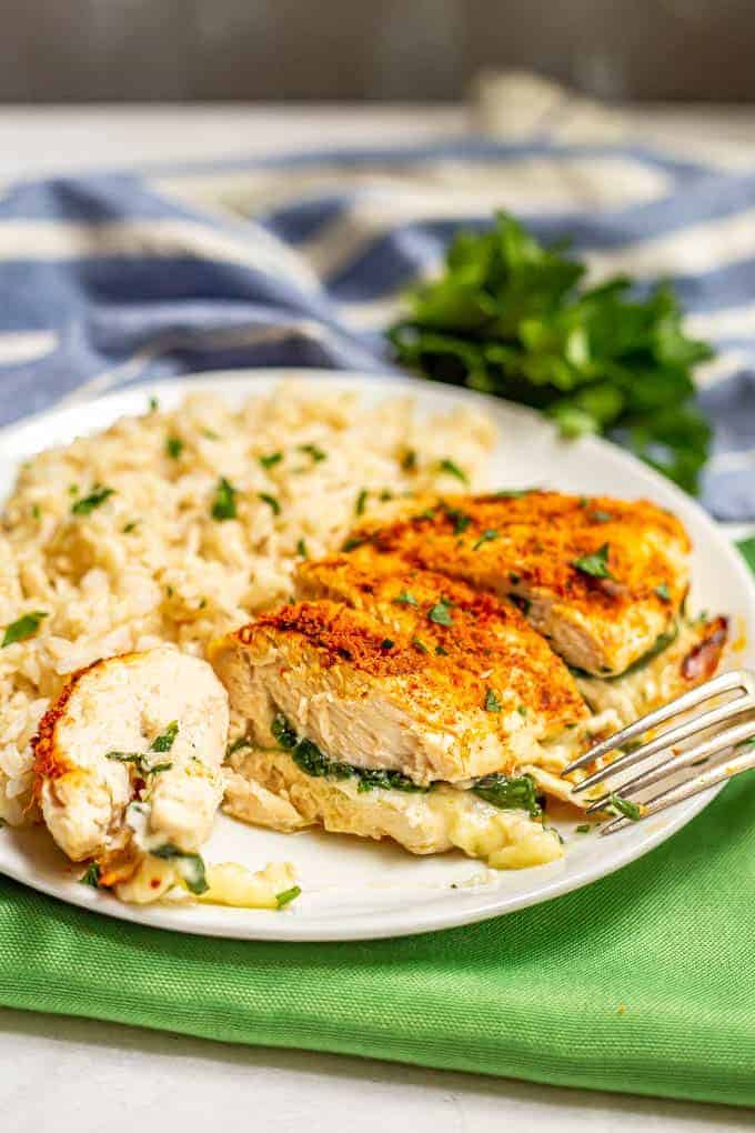 Sliced Parmesan crusted chicken breast stuffed with spinach and mozzarella cheese on a white plate with brown rice and a sprinkling of parsley and a fork nearby