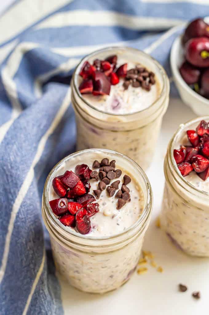 Cherry chocolate chip overnight oatmeal jars with a blue striped towel nearby