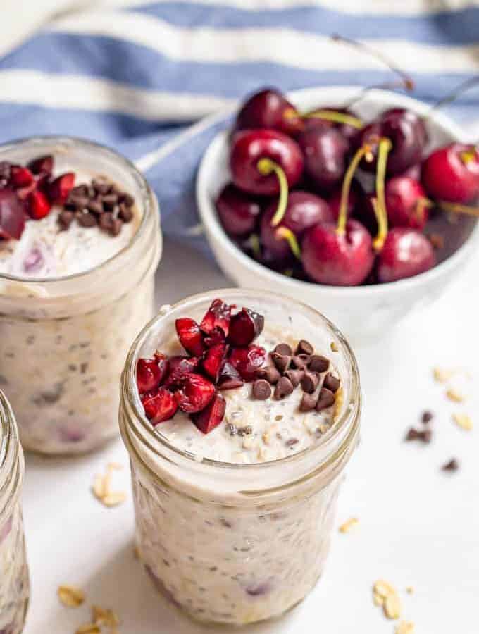 Cherry overnight oats with extra chopped fresh cherries and mini chocolate chips on top in small jars
