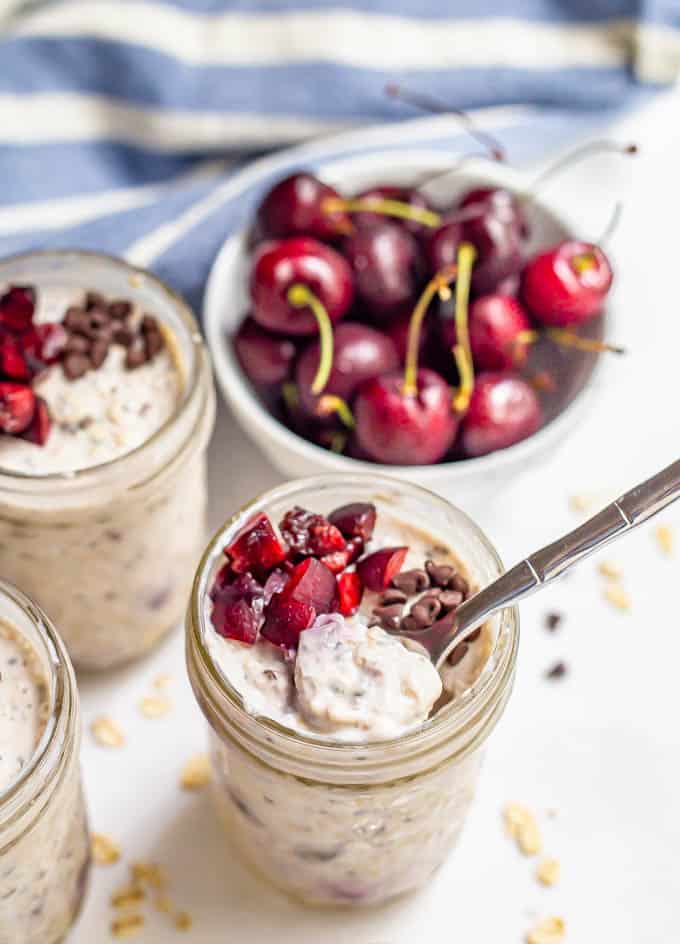 Overnight oats with fresh cherries and mini chocolate chips in small jars with a spoon in one