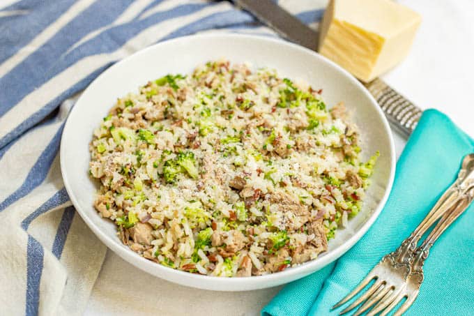 Bowl of rice, broccoli and turkey sausage with Parmesan cheese sprinkled on top and two forks on napkins nearby