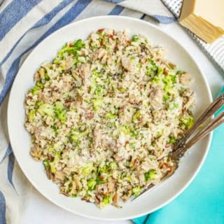 White serving bowl with sausage, rice and broccoli and two forks plus a rind of Parmesan cheese alongside