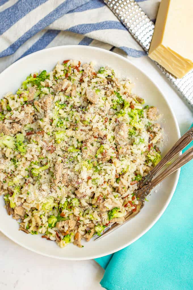 Bowl of wild rice with turkey sausage and broccoli all mixed together with Parmesan cheese on top and two forks alongside