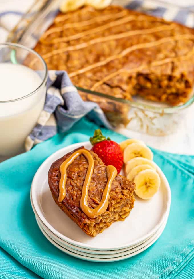 Peanut butter banana baked oatmeal served on a white plate with a drizzle of peanut butter on top and the pan in the background