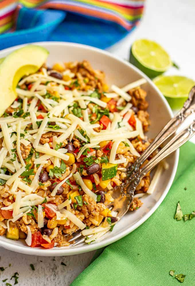 White bowl of ground turkey mixed with rice, beans and veggies with cheese and avocado served with two forks