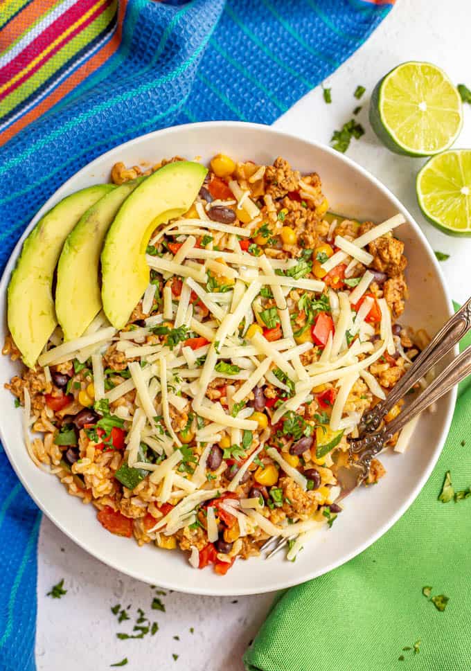 Bowl of ground turkey, rice, beans and veggies with cheese and avocado served with two forks