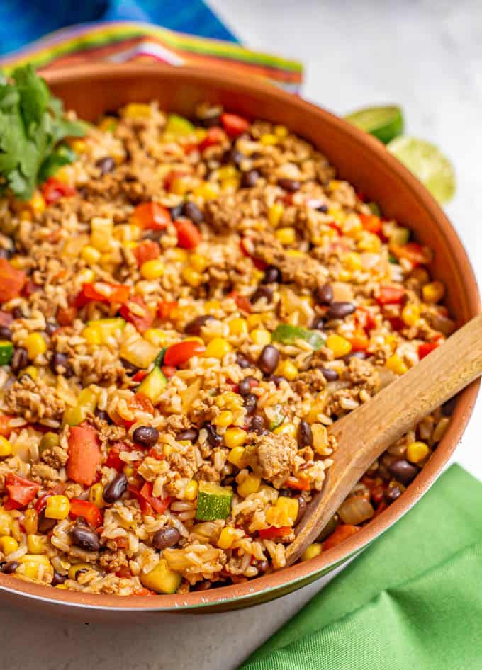 Large skillet with ground turkey, brown rice, black beans and veggies served up with a wooden spoon