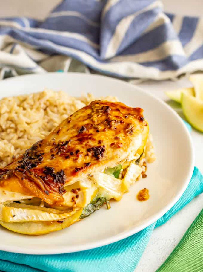 A mustard coated chicken breast with apples and brie served on a white plate with rice