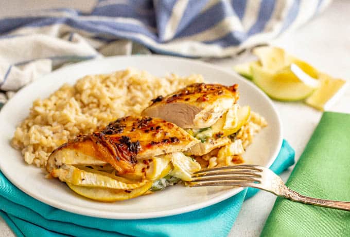 Chicken breast stuffed with spinach, apple and brie cheese cut in half on a white plate with rice served alongside it