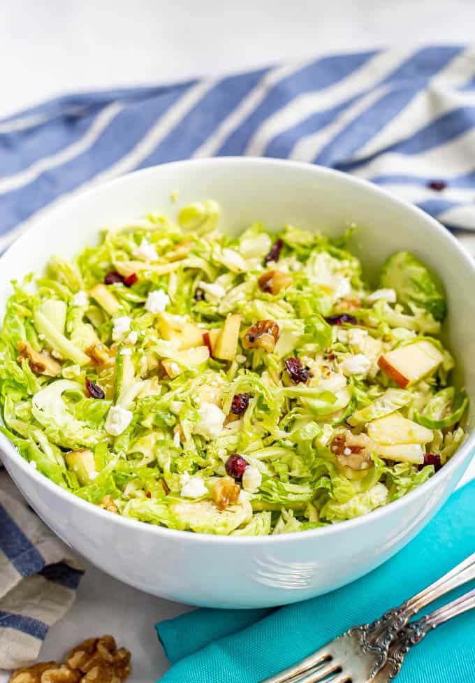 A shredded Brussel sprout salad with apples, walnuts and feta in a large white bowl