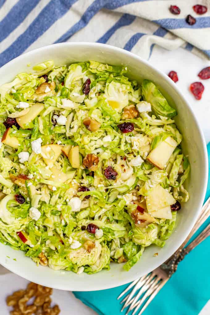 Shaved Brussel sprout salad with apples, walnuts, dried cranberries and feta in a large bowl with towels and napkins nearby