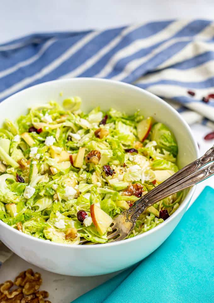 Bowl full of shaved Brussel sprouts with apples, walnuts, dried cranberries and feta and an apple cider vinaigrette