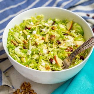 Raw Brussel sprouts shredded into a salad bowl with two forks alongside