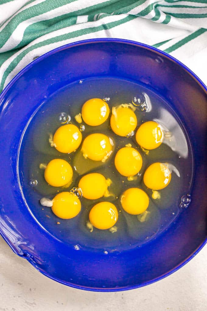 A dozen eggs cracked into a large blue bowl