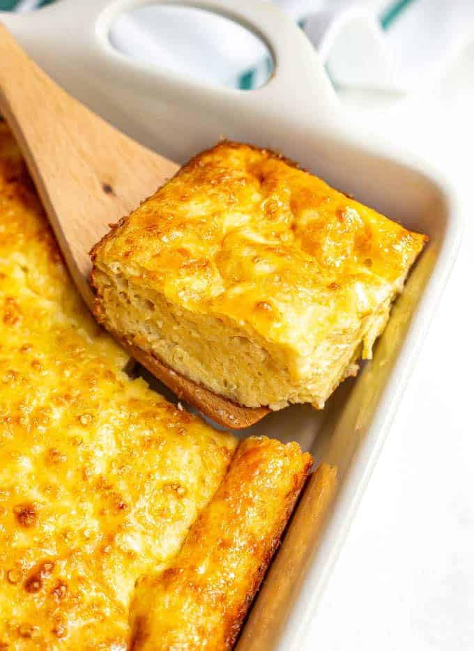 A square of cheesy baked eggs being lifted out of a white casserole dish