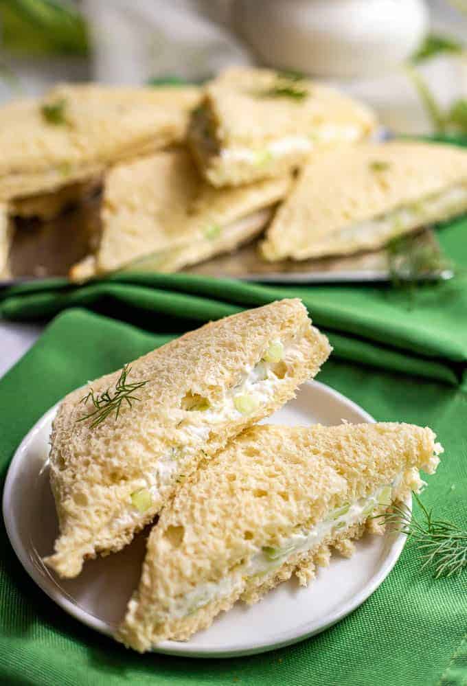 Cucumber tea sandwiches stacked on a small white serving plate with green napkins underneath