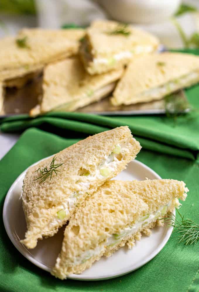 Cucumber tea sandwiches stacked on a small white serving plate with green napkins underneath