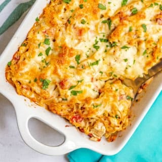 Baked chicken spaghetti casserole with golden brown cheese crusted on top and a sprinkling of parsley and a large spoon taking a scoop