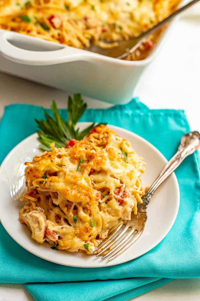 A serving of baked spaghetti with chicken and cream cheese sauce served on a white plate with a fork on the side