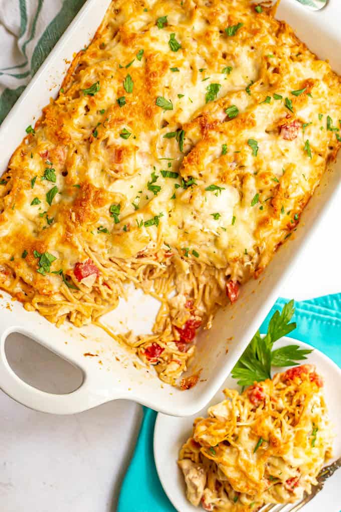 A serving scooped out of baked chicken spaghetti in a casserole dish with the serving plate to the side