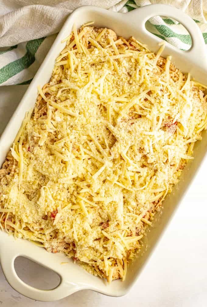 A white casserole dish with chicken spaghetti and two cheeses on top, before being baked