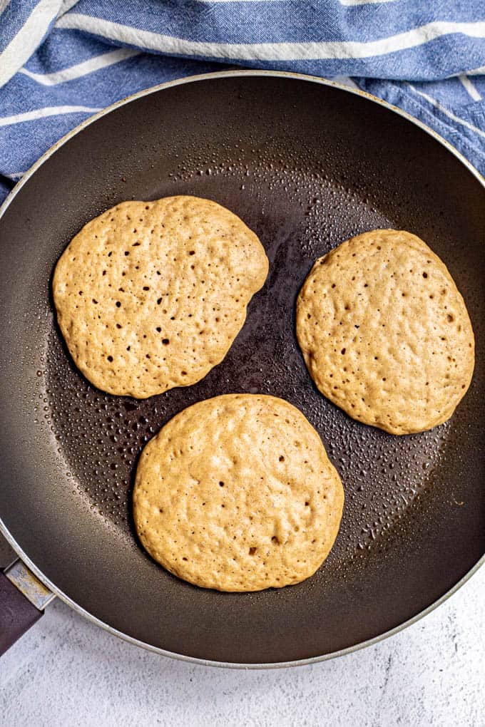 Homemade pancakes cooking in a pan with bubbles on top, before being flipped