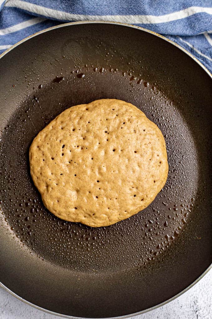 One single large pancake cooking in a pan before being flipped