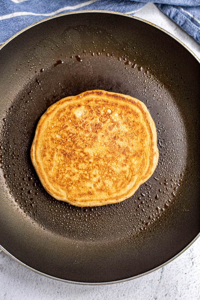 One single large golden brown pancake cooking in a skillet