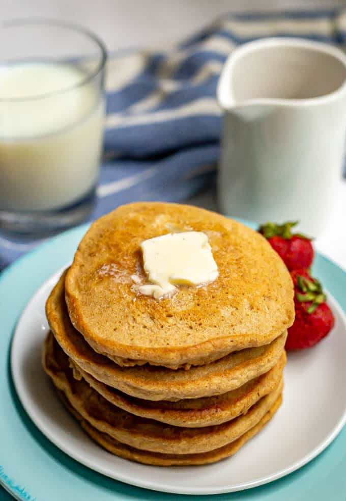 Stack of homemade pancakes with a pat of butter on top served on a white plate with strawberries