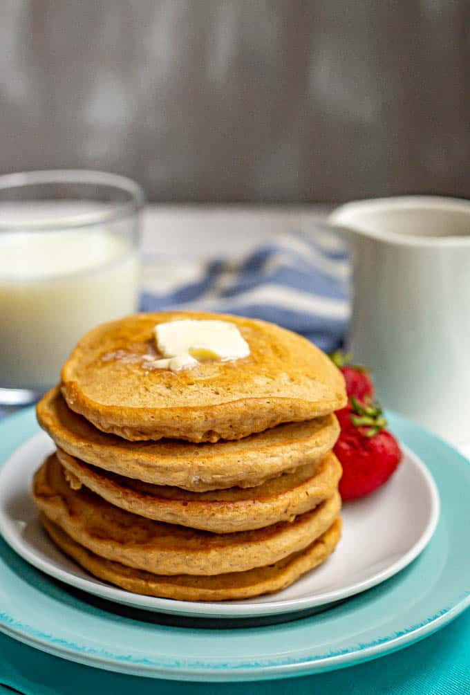 Stack of homemade pancakes with a pat of butter on top served on a white plate with strawberries