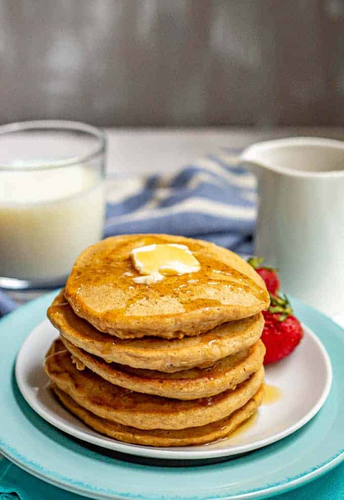 Stack of whole wheat pancakes served on a plate with a pat of butter on top and maple syrup drizzled over