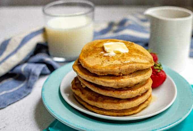 Stack of whole wheat pancakes with a pat of butter on top and maple syrup drizzled over