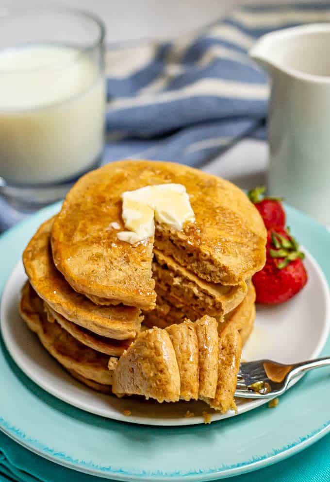 Stack of pancakes with a forkful taken out and laying on the side of the plate