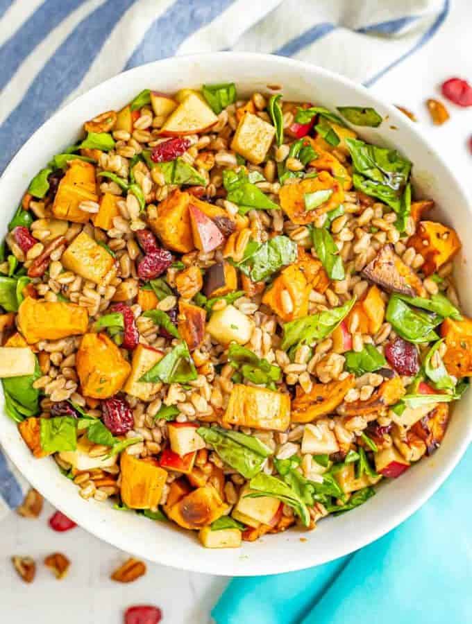 A harvest farro salad with sweet potatoes, spinach, pecans and apples in a large white bowl