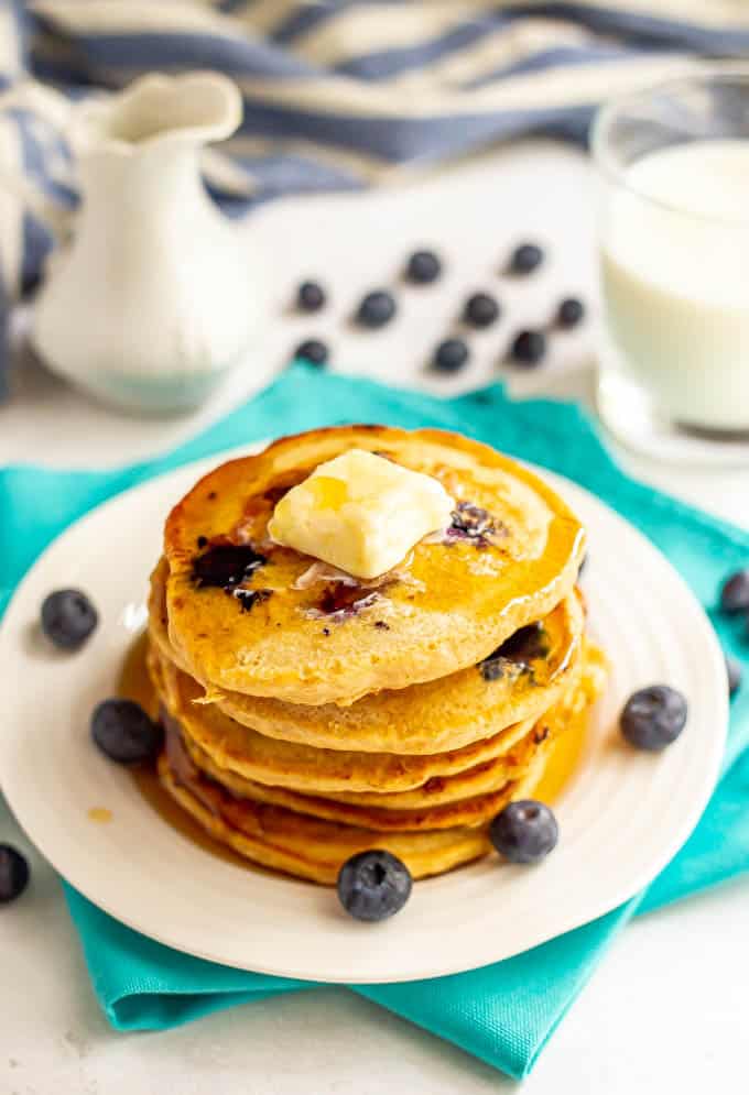 A stack of healthy blueberry pancakes with a pat of butter on top and a drizzle of maple syrup