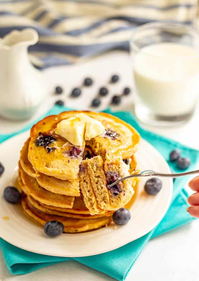 A forkful of blueberry pancakes being taken out of a stack on a white plate