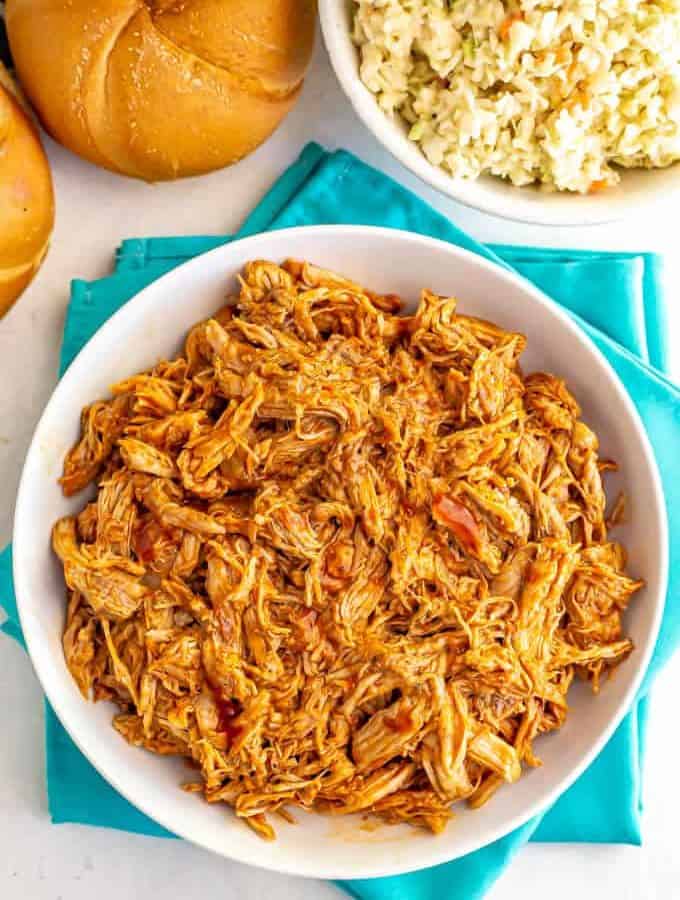 Large white bowl of shredded Instant Pot pulled pork with BBQ sauce and a side of coleslaw