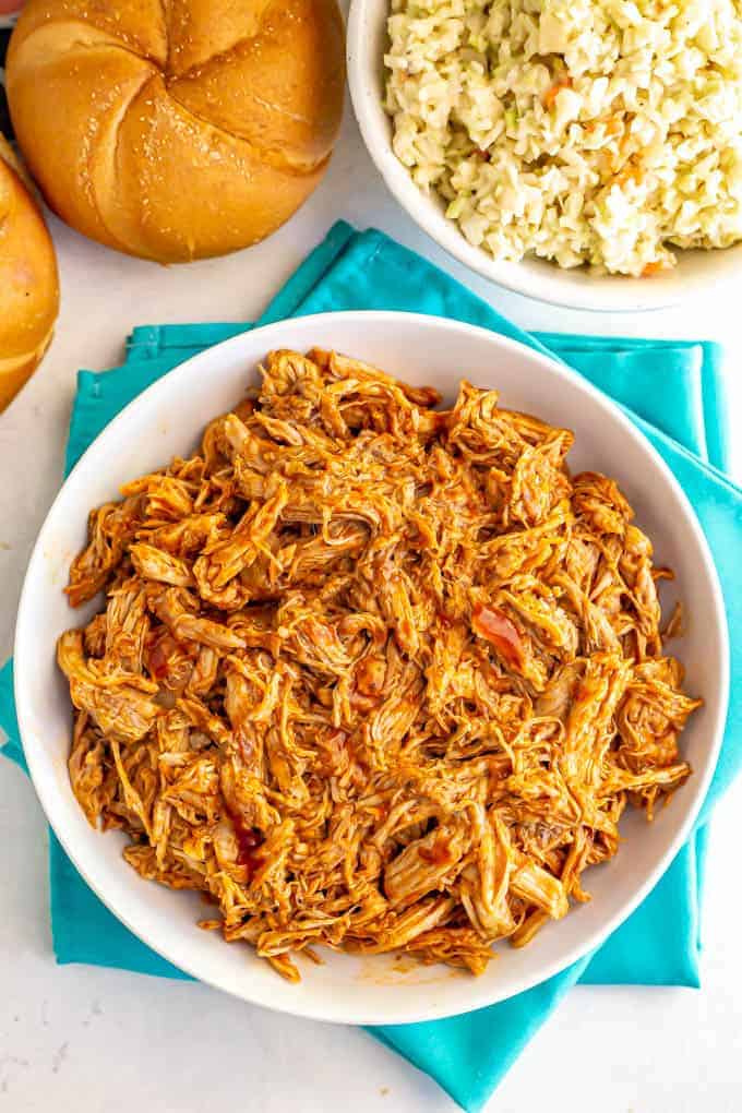 Large white bowl of shredded Instant Pot pulled pork with BBQ sauce and a side of coleslaw