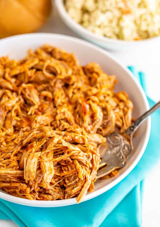 A bowl of shredded pulled pork with a serving fork on the side